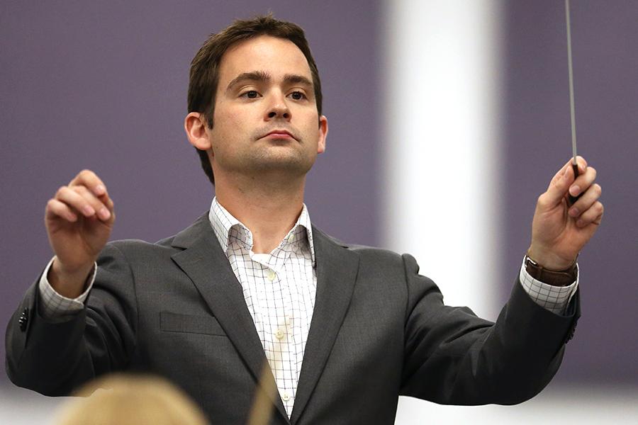 A person wearing a suit jacket raises their hands to conduct.