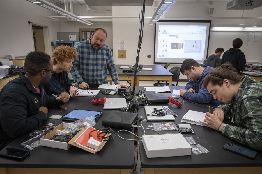 Students work with a faculty member as they build circuitry at a large table.