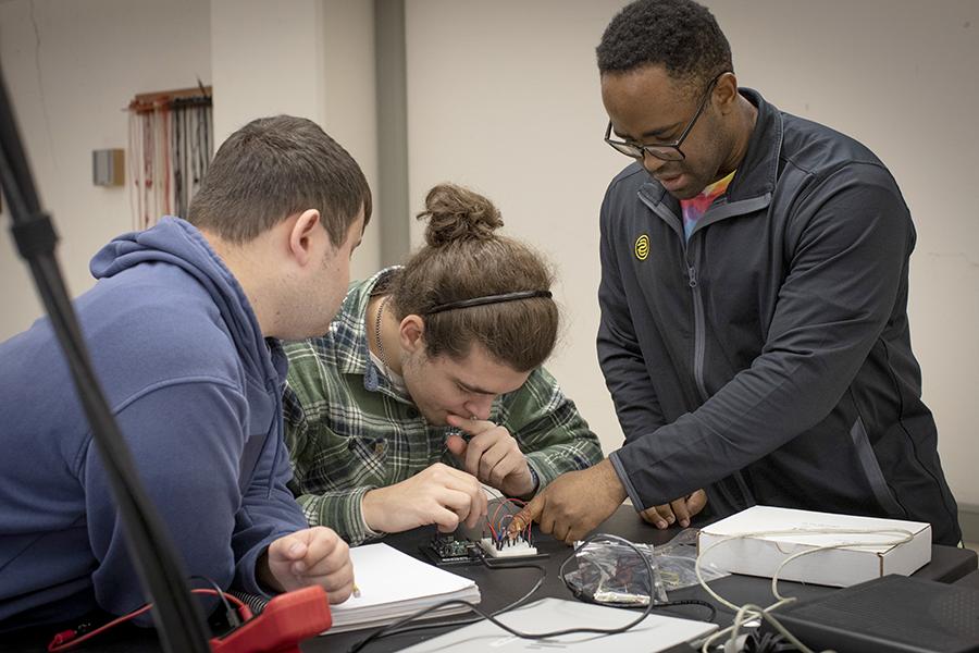 Three students work together in a lab classroom and work on building wire circuits.